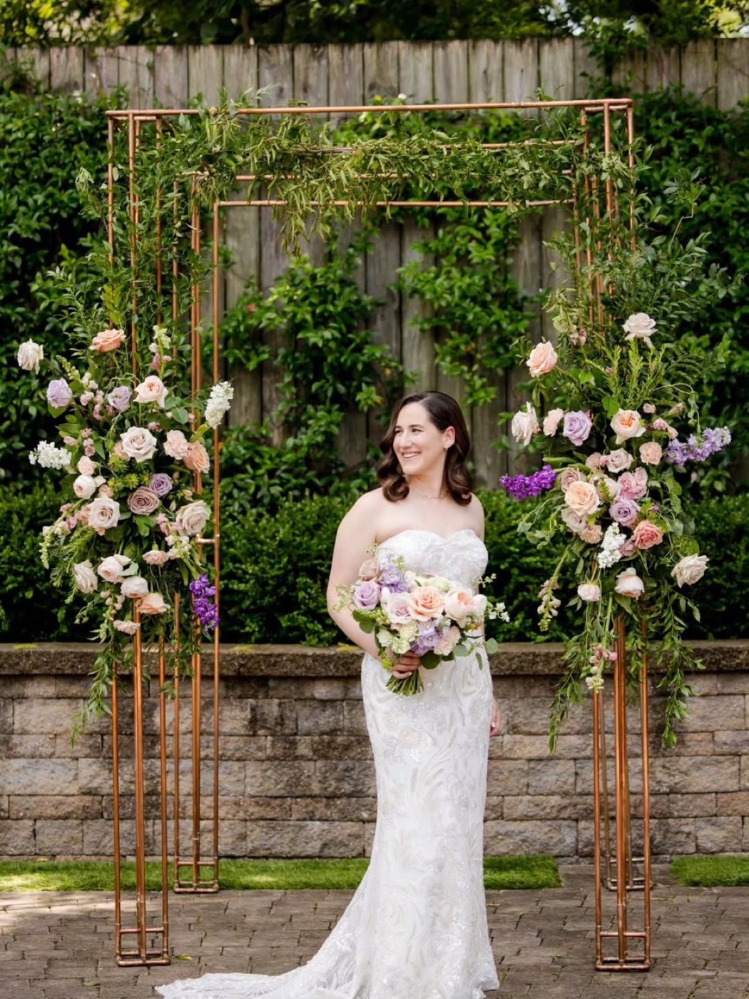 Bride standing under the copper chuppah with pastel rose arrangements on each post